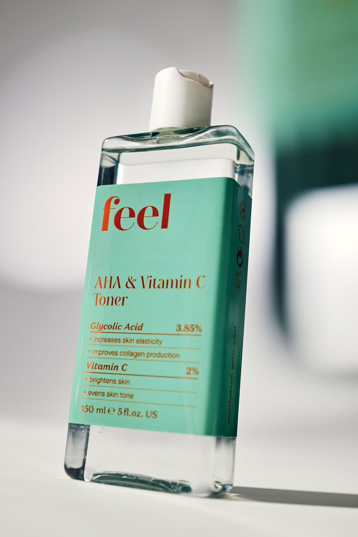A clean rectangular bottle with a teal label that says "AHA & Vitamin C Toner" stands in the centre of a grey background. The image is taken at an angle.