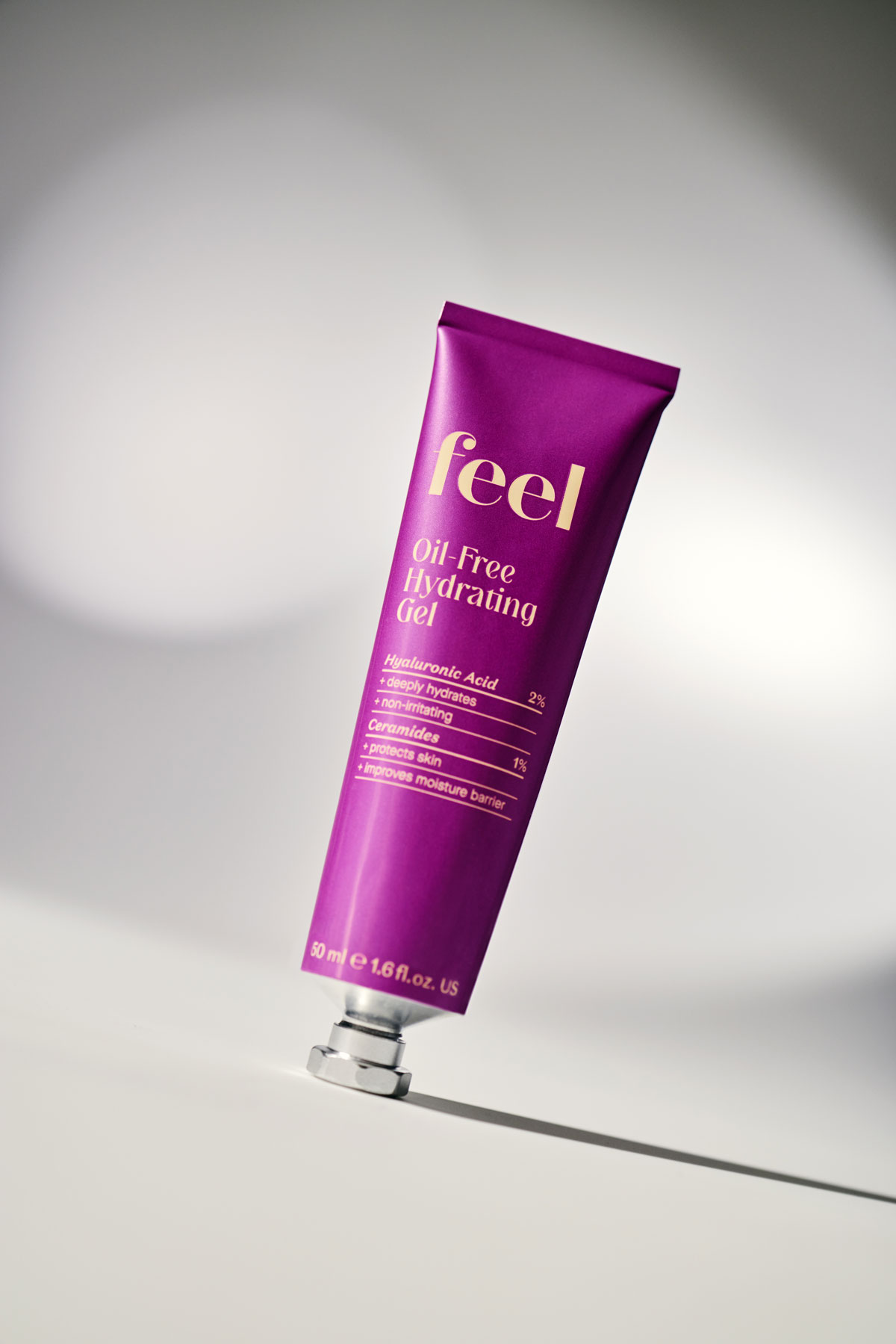 Metallic magenta coloured aluminum tube that says "Oil-Free Hydrating Gel" in flat light yellow text. Flat table plane is set on an angle.
